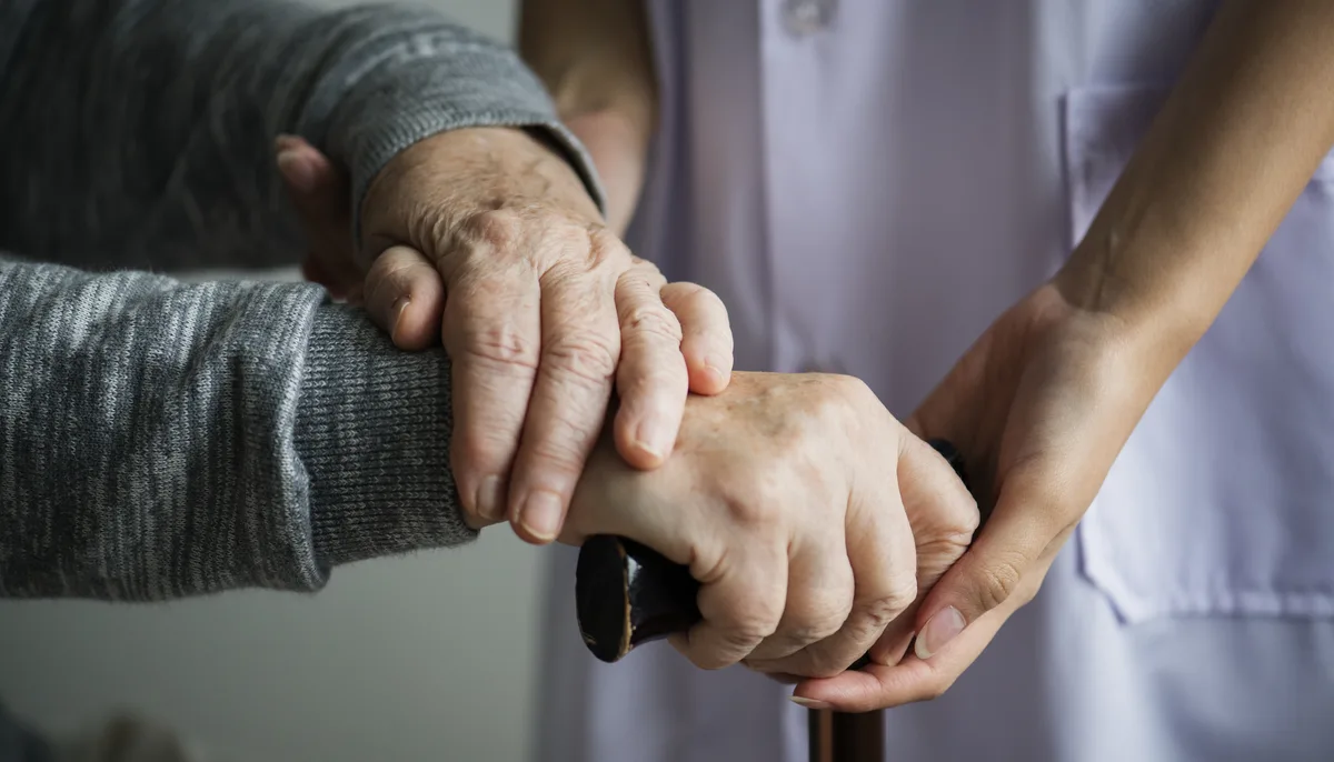 Eine helfende Hand stützt die Hand eines älteren Menschen am Gehstock – Symbol für die Entlastung pflegender Angehöriger
