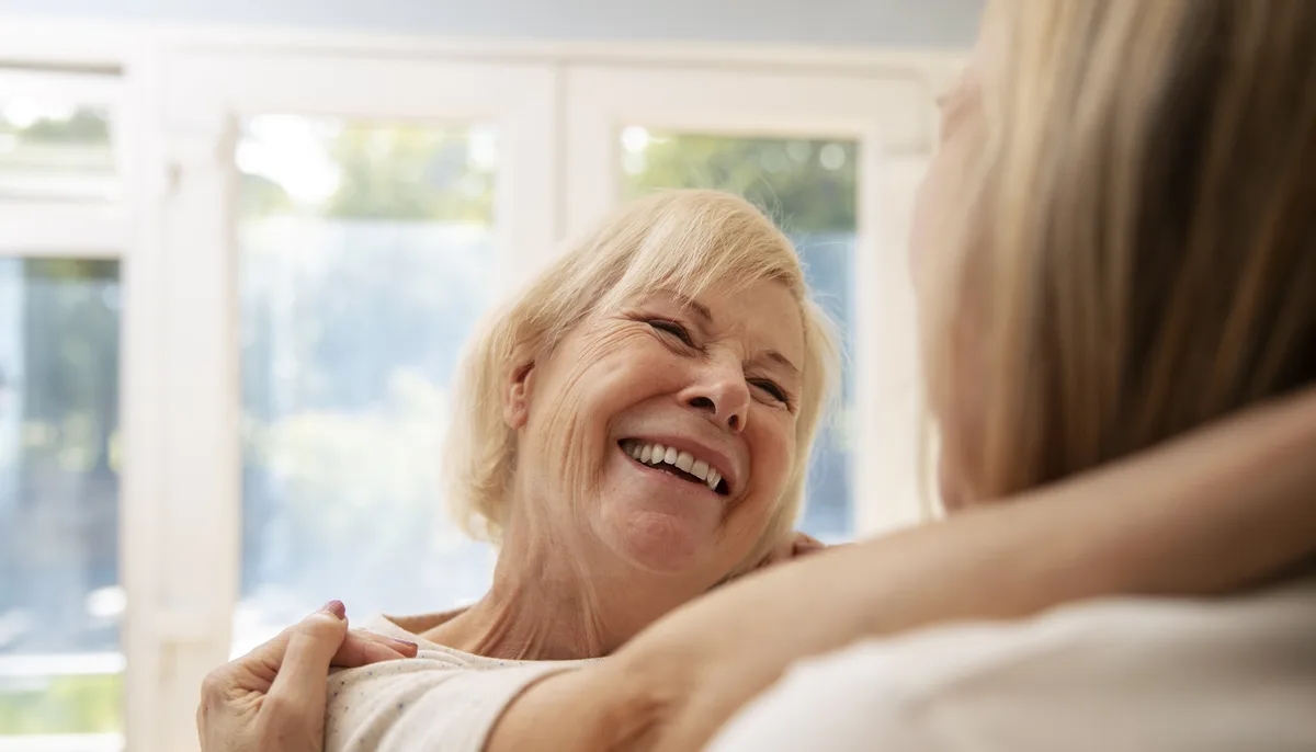 Lachende Seniorin wird zu Hause von einer jüngeren Angehörigen umarmt – Ankommen nach dem Klinikaufenthalt